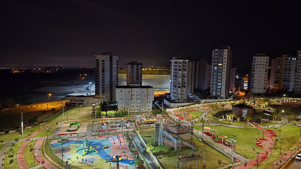 Gece manzarasında, park ve apartmanların olduğu aydınlatılmış bir şehir alanı.